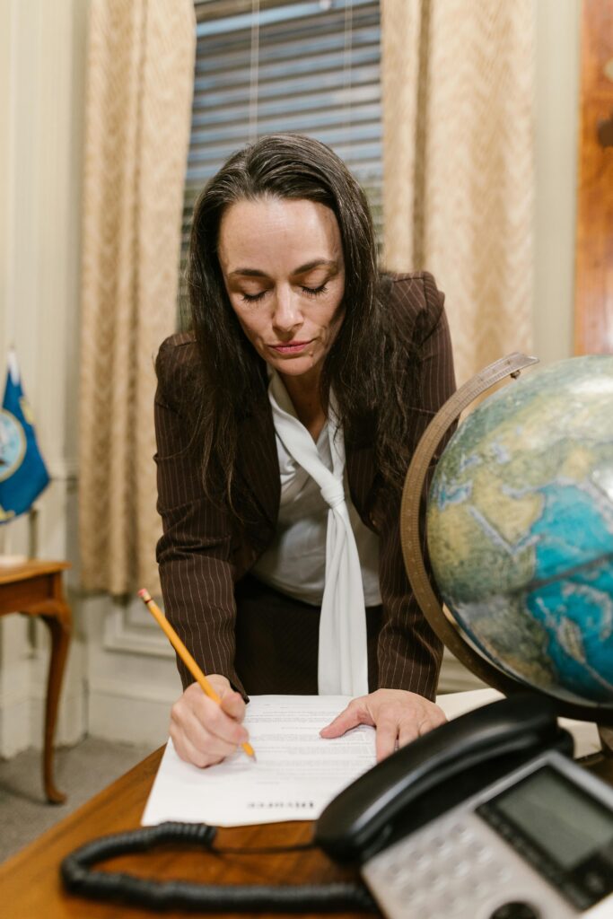A woman in formal attire writes on documents in an office, symbolizing professionalism and business.