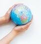 A close-up of hands gently holding a colorful globe against a white background.