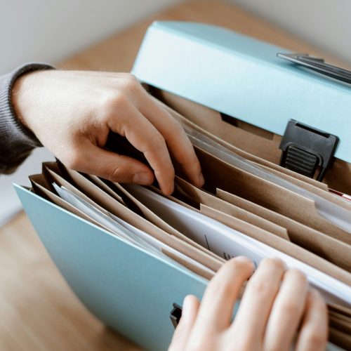 Close-up of hands organizing papers in a blue folder, ideal for business and office concepts.