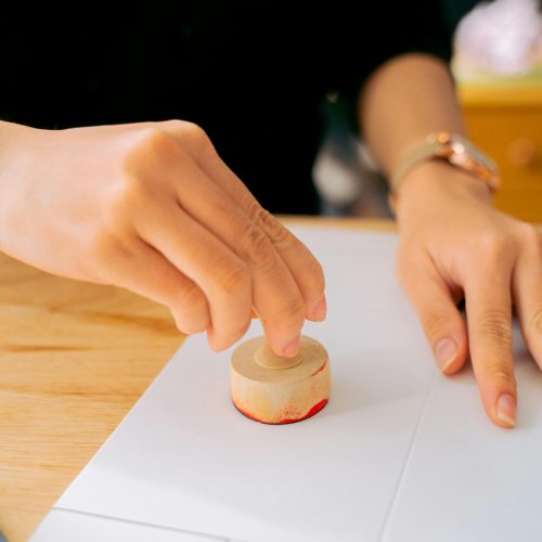 Close-up of a person using a wooden stamp on white paper indoors.